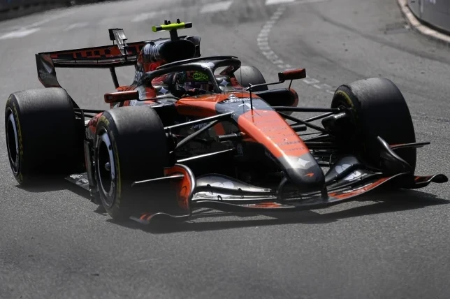 Formula 1 bolid u boji narandže i crne boje kako prolazi kroz krivinu na trkačkoj stazi.
