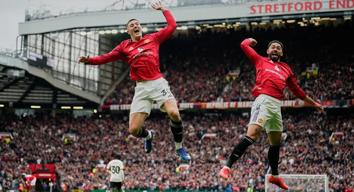Dva fudbalera u crvenim dresovima Manchester Uniteda skaču u zrak slaveći postignuti gol, na punom stadionu Old Trafford.