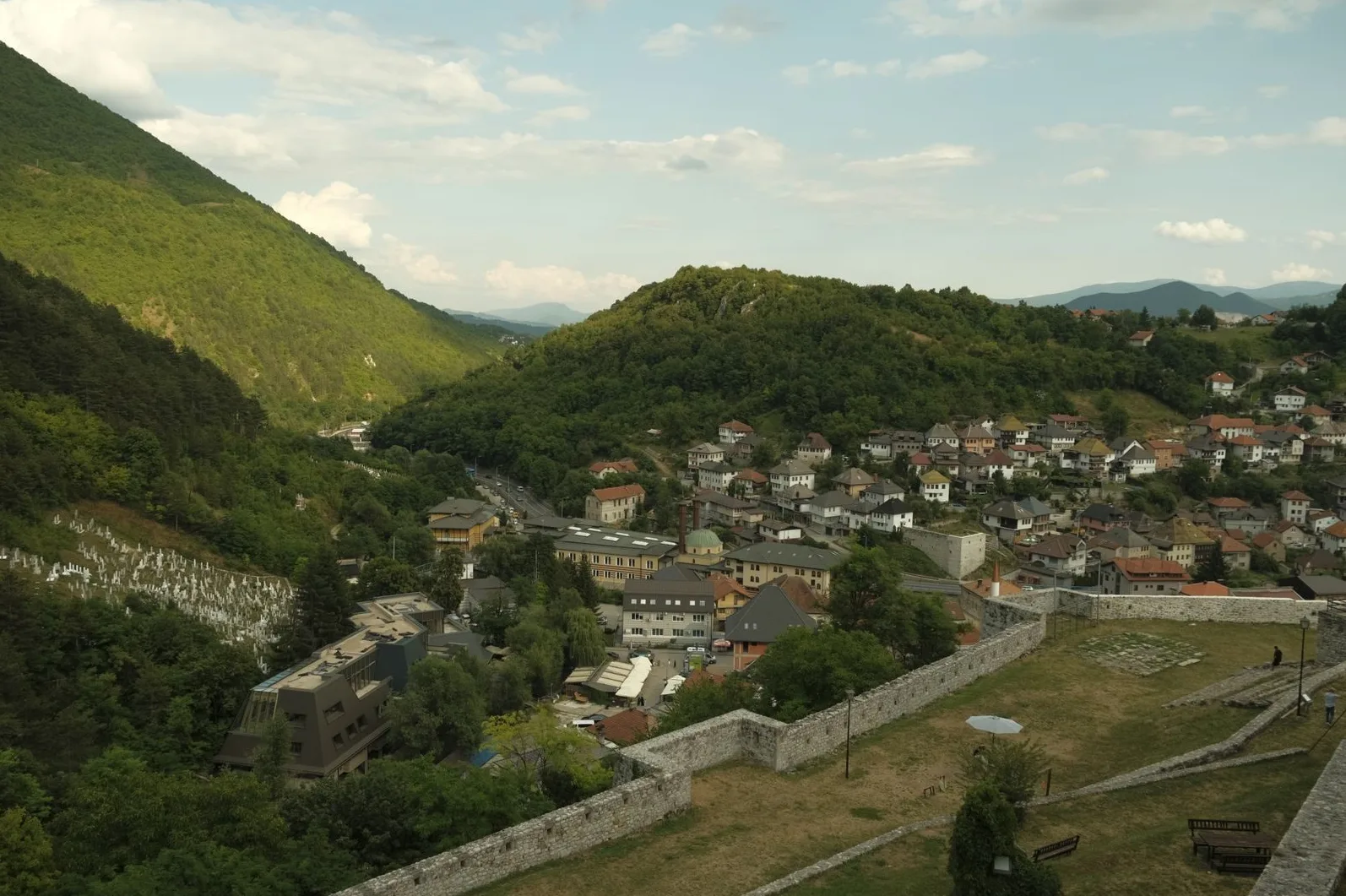 Panoramski pogled na grad smješten u dolini, okružen brdima prekrivenim bujnim zelenilom.