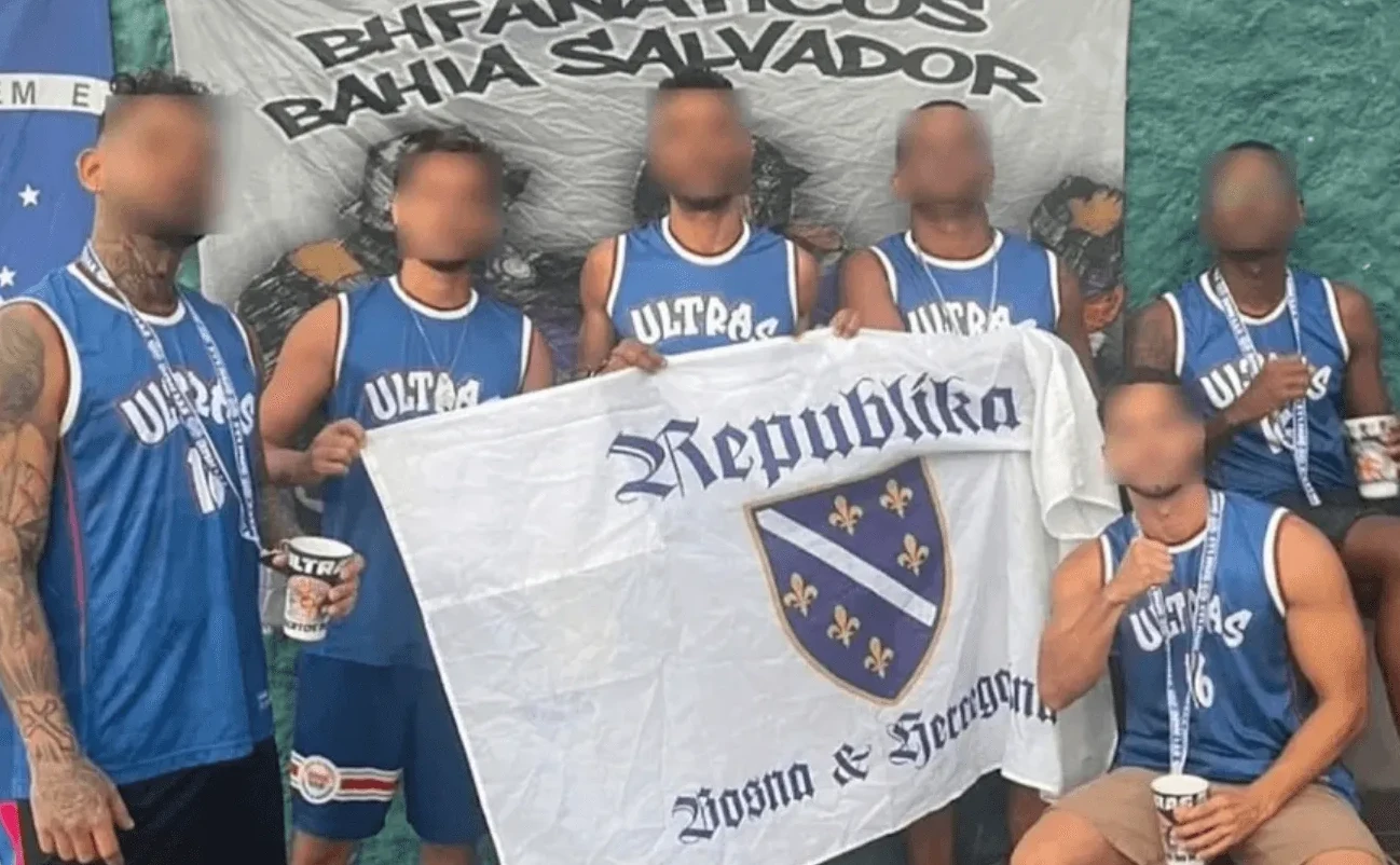 Grupa muškaraca u plavim majicama sa natpisom "ULTRA" drži zastavu Bosne i Hercegovine.