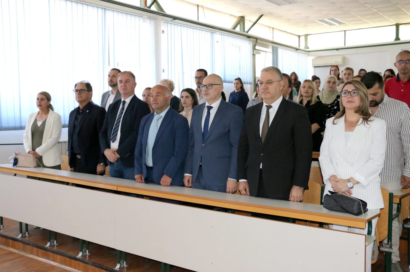Grupa ljudi u svečanoj odjeći stoji ispred radne ploče u moderno uređenoj učionici.