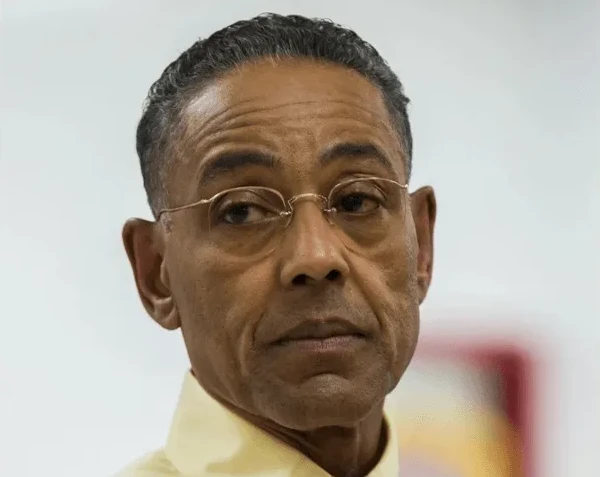 Gus Fring nosi naočare i žutu košulju, ozbiljnog izraza lica.