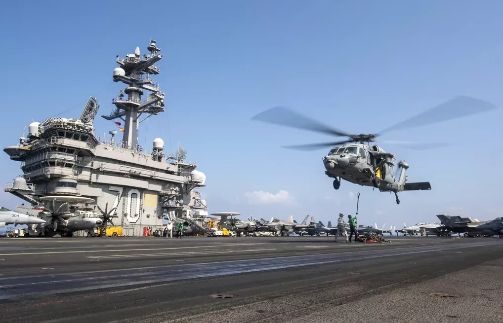 Helikopter slijeće na palubu nosača aviona.