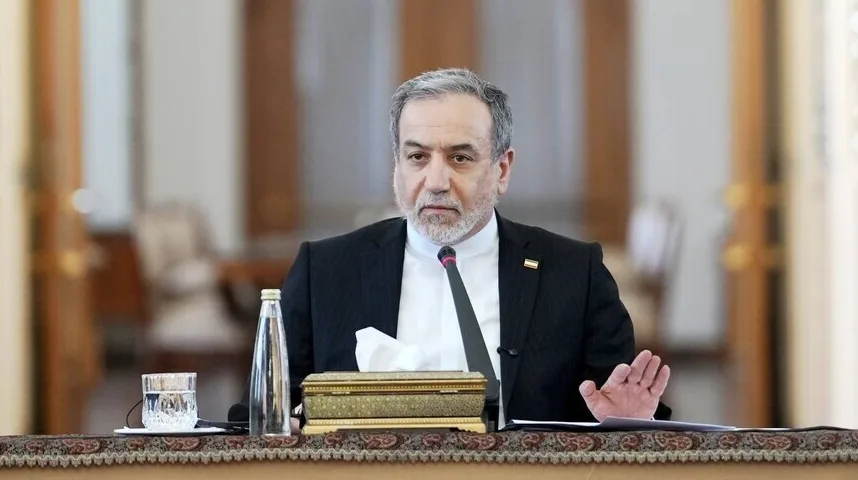 Iranski diplomata sa sijedom kosom i bradom, obučen u crno odijelo, sjedi za stolom ispred mikrofona, držeći podignutu ruku u gestu objašnjenja.