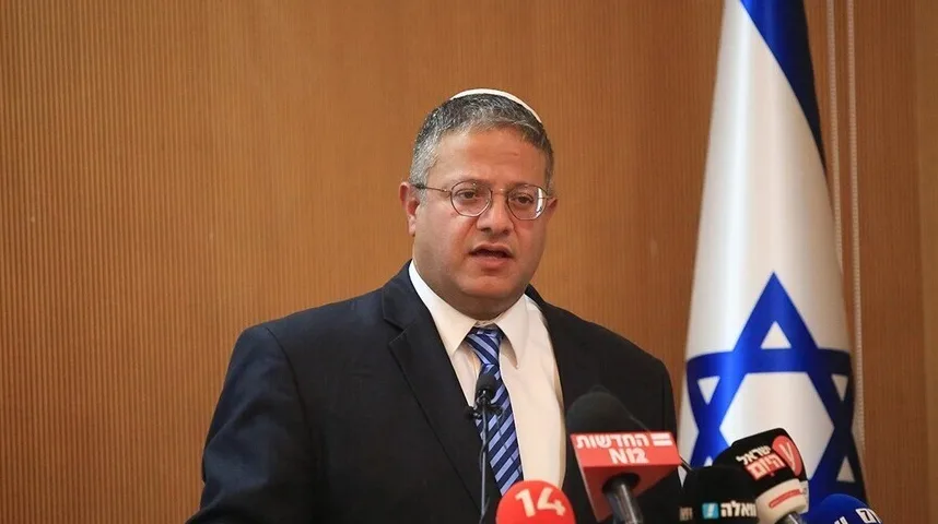 Izraelski zvaničnik u crnom odijelu i plavoj kravati, sa tradicionalnom jevrejskom kapicom na glavi, obraća se novinarima pored zastave Izraela.