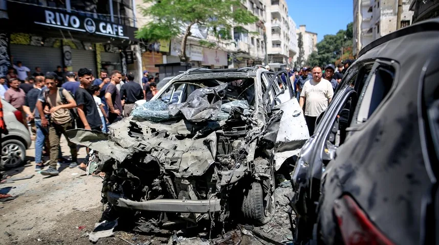 Potpuno uništen bijeli automobil nakon eksplozije, saobraćajnica zatrpana krhotinama, ljudi promatraju prizor.