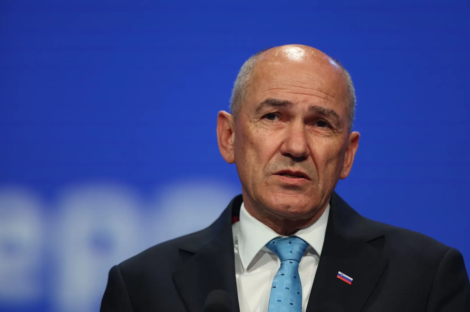 Portret Janeza Janše, bivšeg premijera Slovenije, sa plavom kravatom i zastavicom Slovenije na reveru.