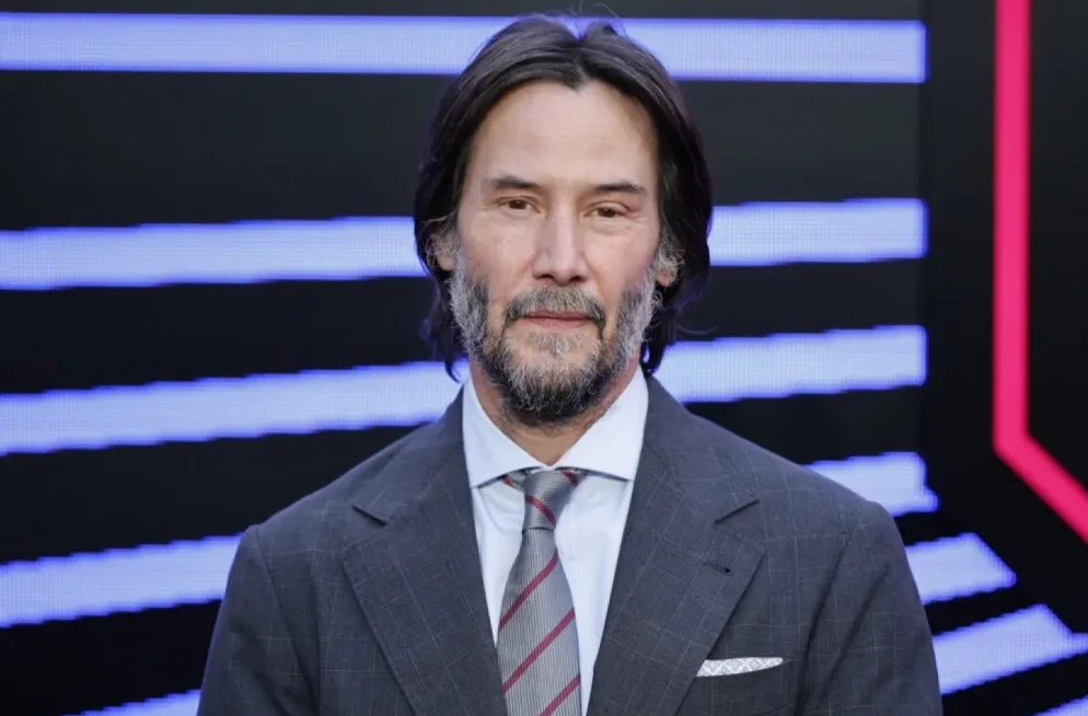 Keanu Reeves u tamnom odijelu i sa sivom kravatom sa crvenim prugama