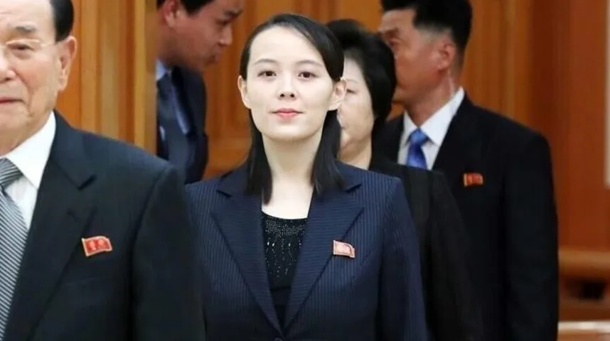Kim Yo-jong nosi tamno odijelo s brošem dok stoji među sjevernokorejskim zvaničnicima.