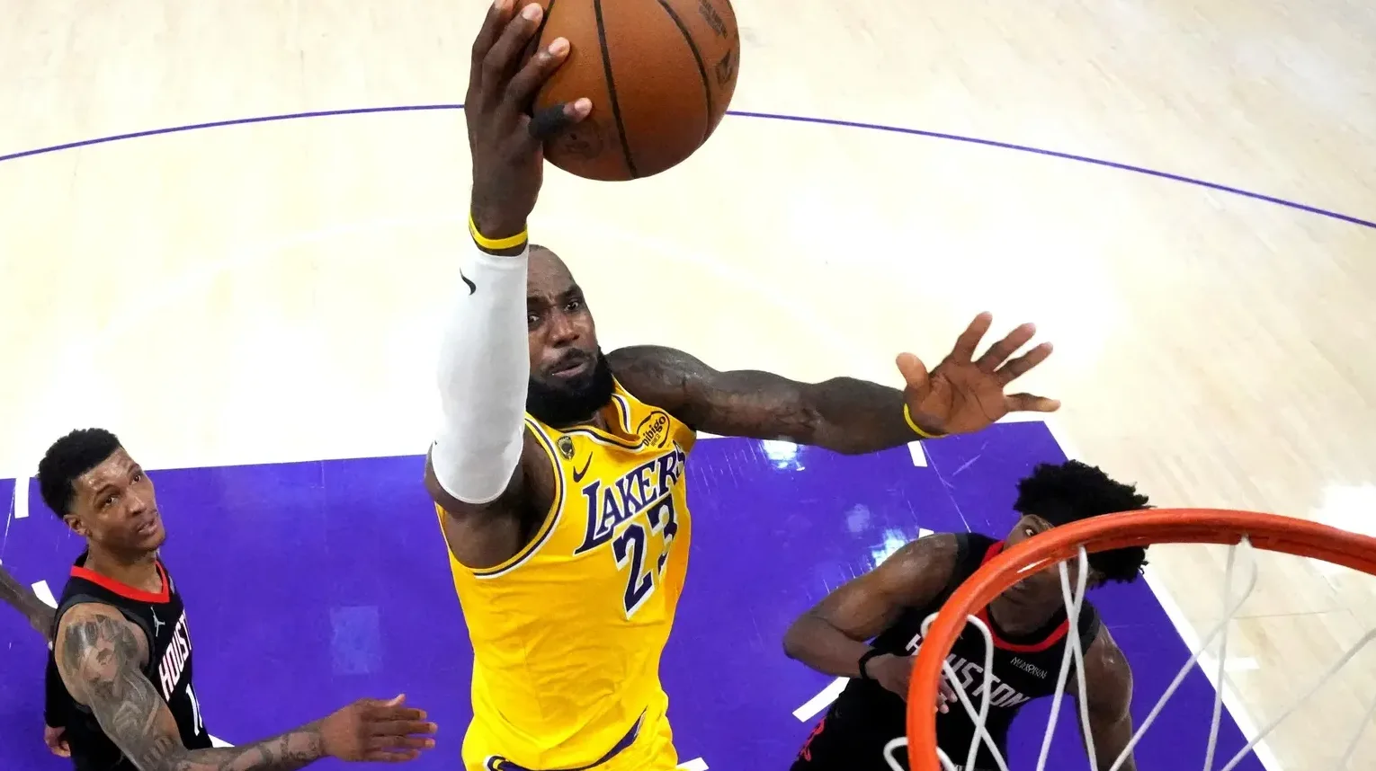 LeBron James u žutom dresu Los Angeles Lakers sa brojem 23 zakucava loptu u koš dok ga dvojica igrača u crnim dresovima pokušavaju blokirati.