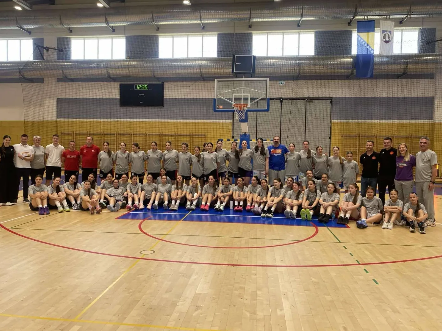 Sastav košarkaškog tima sa trenerima u sportskoj dvorani, poziraju za fotografiju.