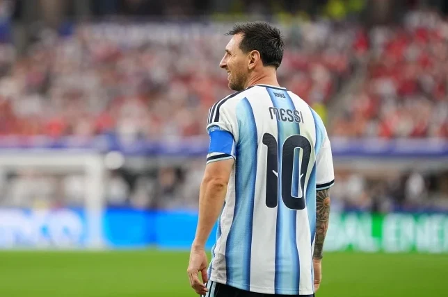Lionel Messi, fudbaler Argentine, nosi dres sa brojem 10 i prezimenom 'Messi' na leđima, sa plavom trakom na ruci, na zelenom fudbalskom terenu.