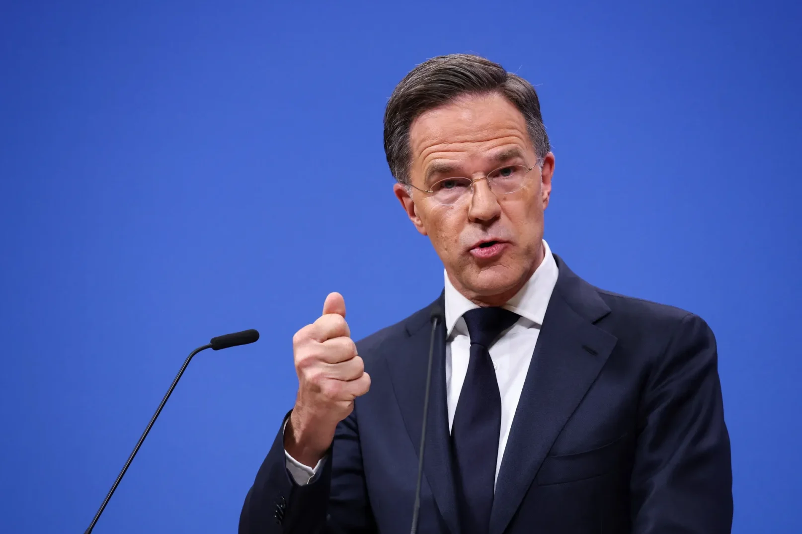 Mark Rutte, premijer Holandije, drži palac gore ispred mikrofona na plavoj pozadini.
