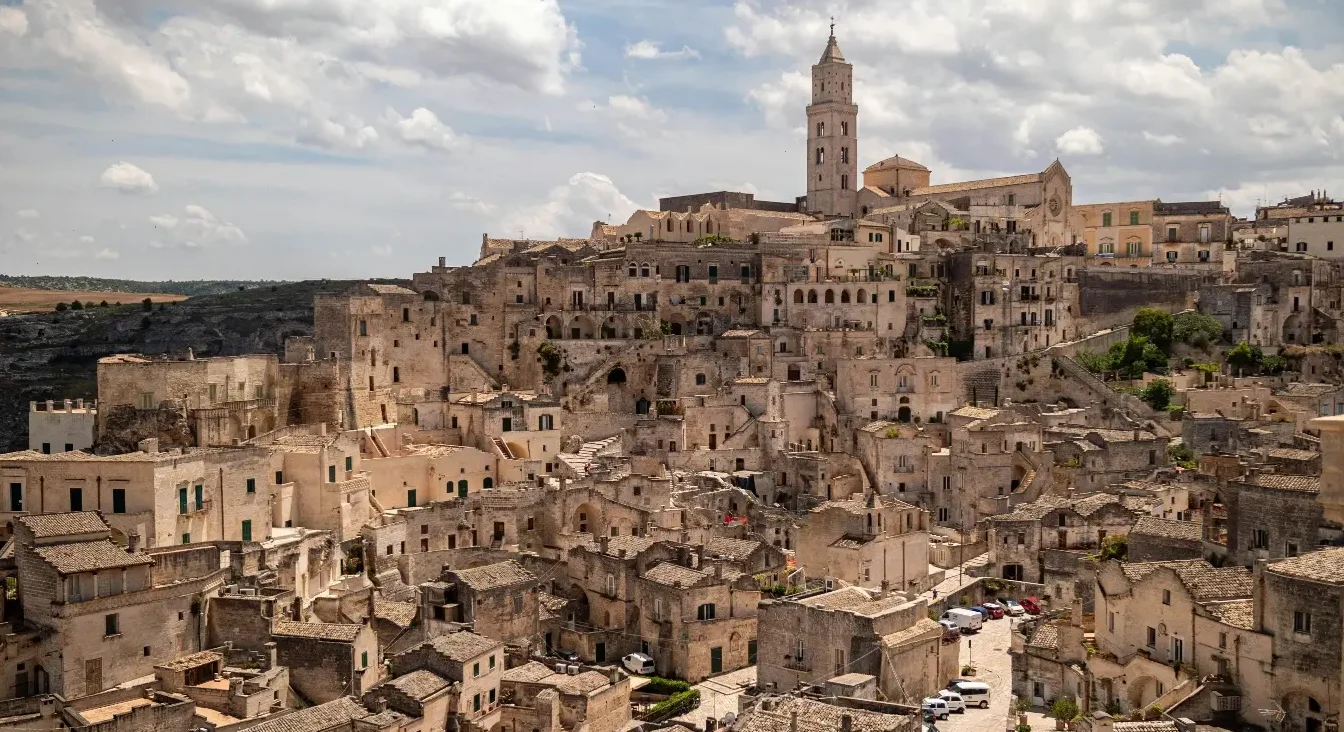 Panoramski pogled na drevni kameni grad Materu u Italiji s karakterističnim kućama uklesanim u stijene i srednjovjekovnim tornjem crkve.