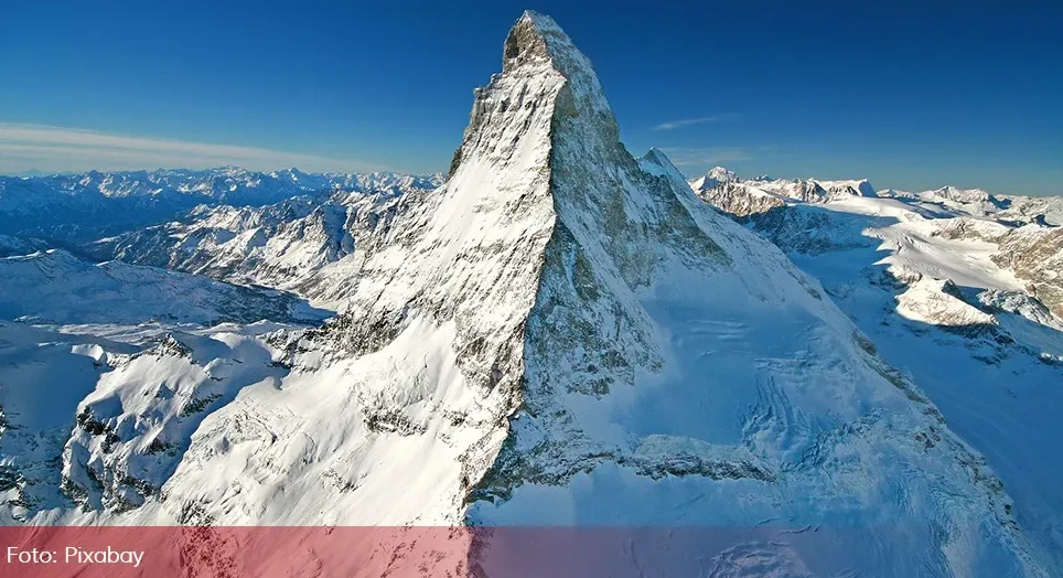 Fotografija sniježnog vrha planine Materhorn na jasnom plavom nebu, okružena drugim planinskim vrhovima prekrivenim snijegom.