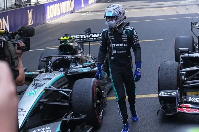 Vozač Formule 1 u Mercedesovom kombinezonu pored bolida na stazi.
