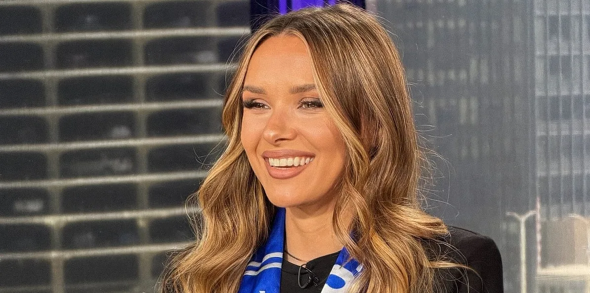 Mlada žena sa smeđom kosom i osmijehom nosi plavi šal sa bijelim prugama i crnu jaknu.
