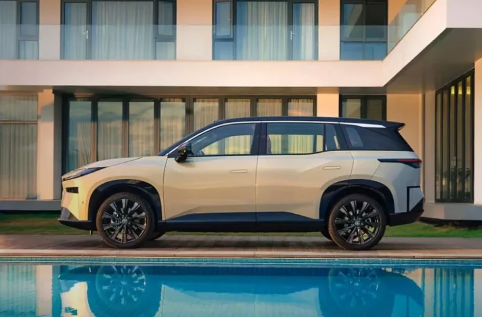 Zlatno-bež električni SUV vozilo u profilu, parkiran pored bazena sa plavom vodom.