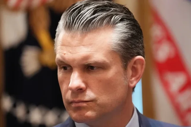 Portret muškarca u tamnom odijelu, s naglašenom sijedom kosom očešljanom unazad.