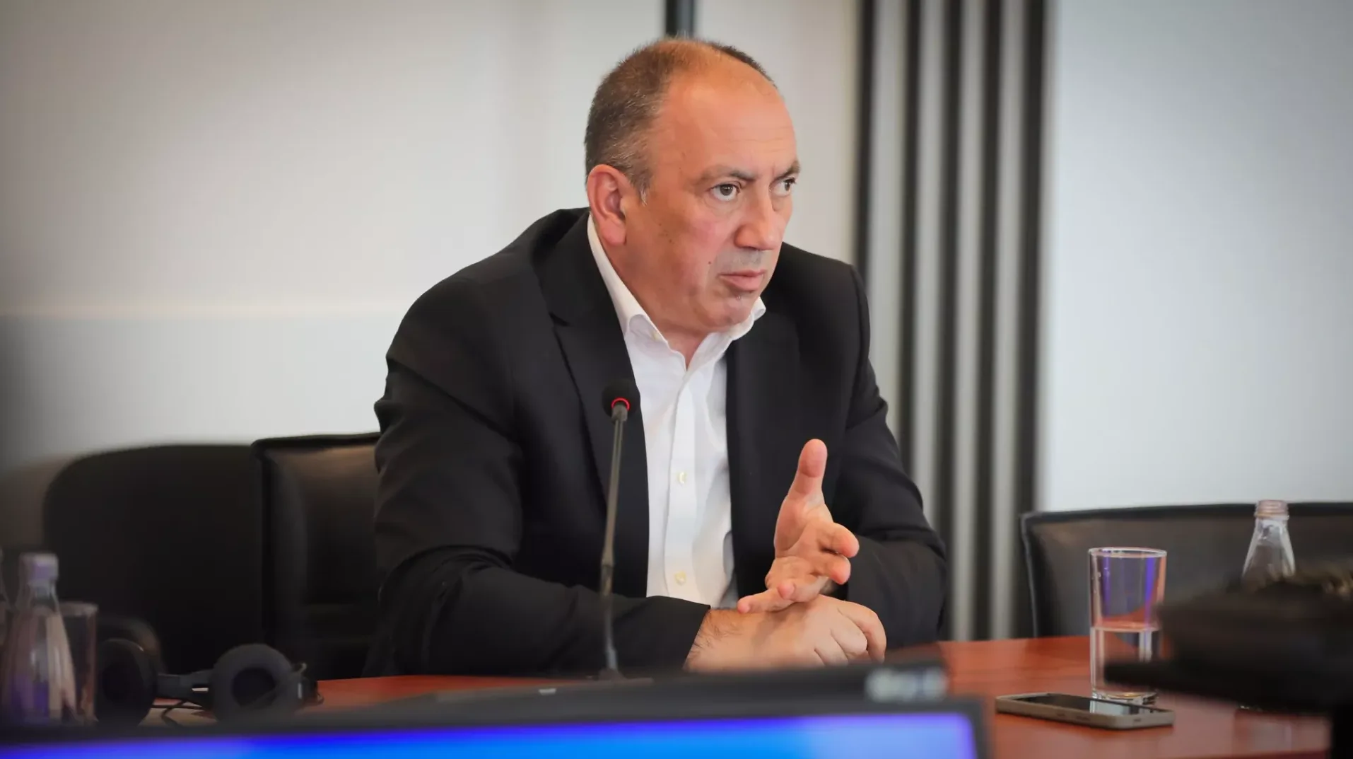 Muškarac u crnom odijelu i bijeloj košulji govori za mikrofonom.