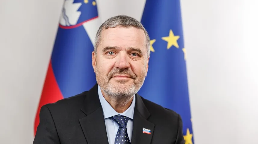 Portret muškarca u tamnom odijelu, plavoj košulji i plavoj kravati sa dezenom, koji stoji ispred zastava Slovenije i Evropske unije.