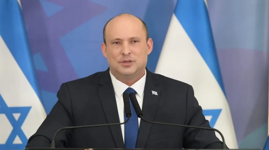 Naftali Bennett, bivši premijer Izraela, u odijelu sa plavom kravatom i zastavom Izraela u pozadini