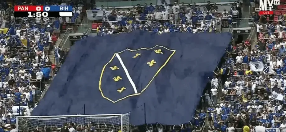 Fudbalski navijači Bosne i Hercegovine razvijaju veliku plavu zastavu sa grbom BiH na tribinama stadiona.