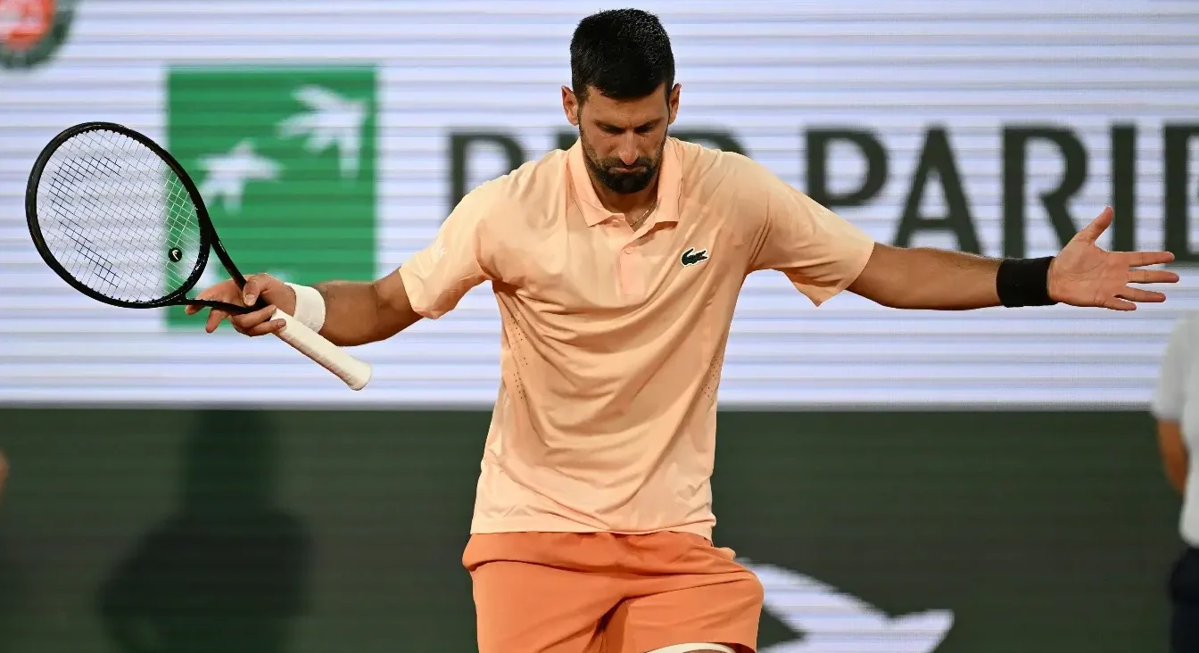 Novak Đoković u narandžastoj majici i šorcu, drži reket u jednoj ruci, sa podignutim rukama i izrazom lica koji pokazuje emocije nakon osvojenog poena na Rolan Garosu.