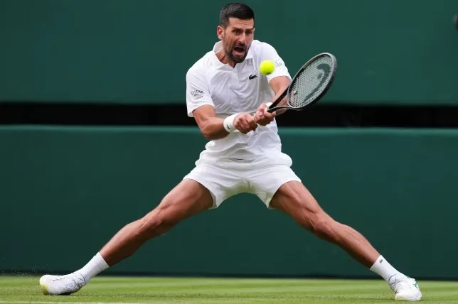 Novak Đoković u bijelom dresu i šorcu, sa reketom u ruci, kako iz sve snage udara tenisku lopticu na travi Vimbldona.