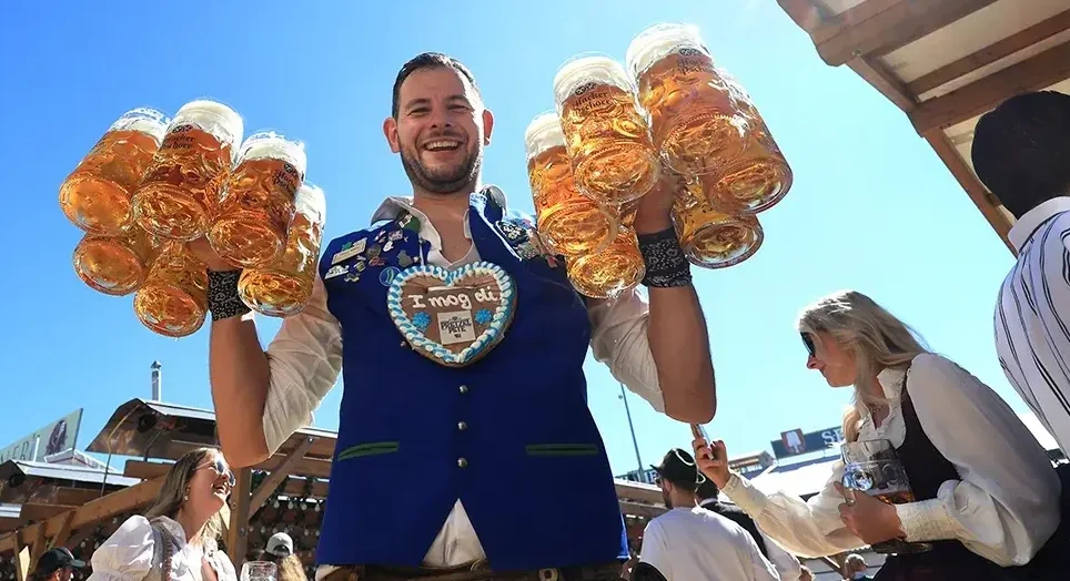 Nasmijani muškarac u narodnoj nošnji drži više velikih krigli piva.