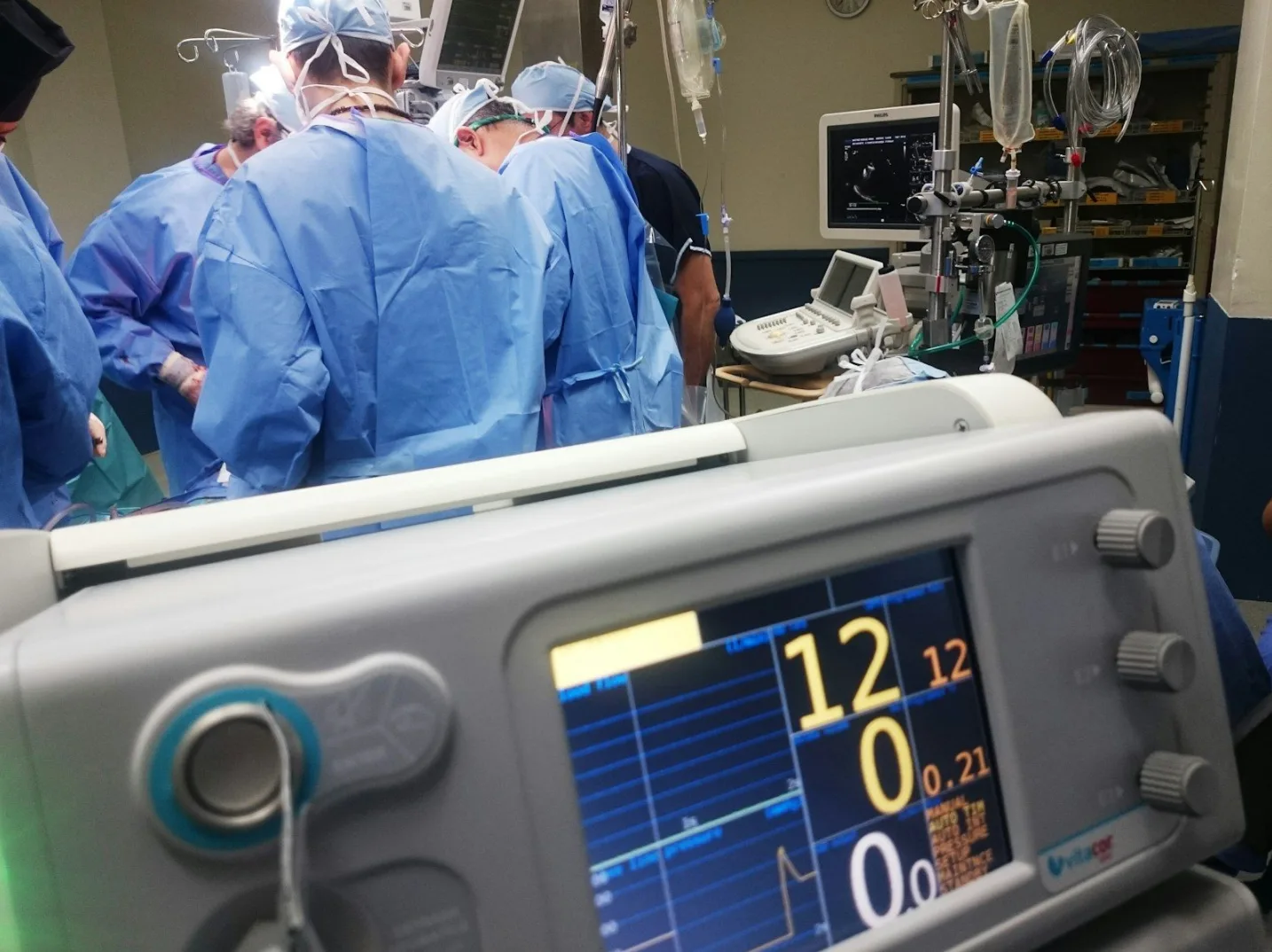 Hirurški tim u plavim uniformama obavlja operaciju, sa fokusom na monitor medicinskog aparata.