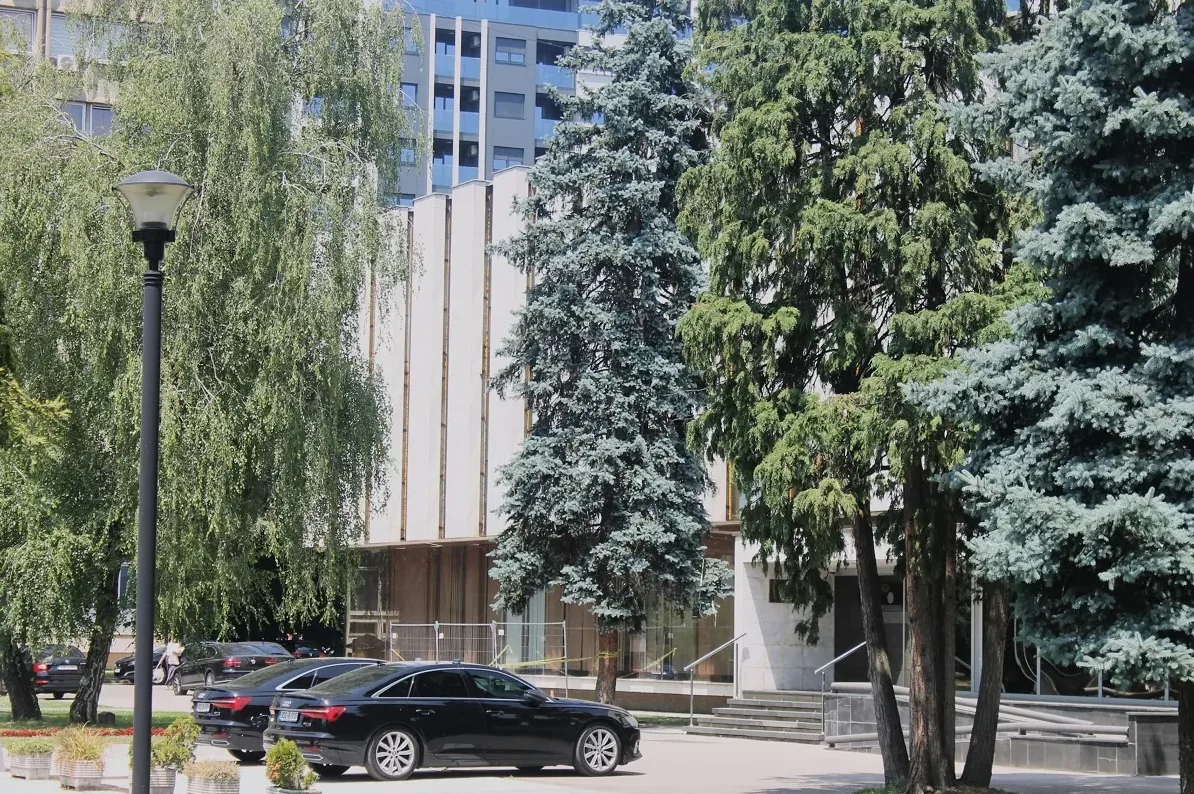 Crni Audi automobili parkirani ispred moderne zgrade sa stubištem, okruženi drvećem.