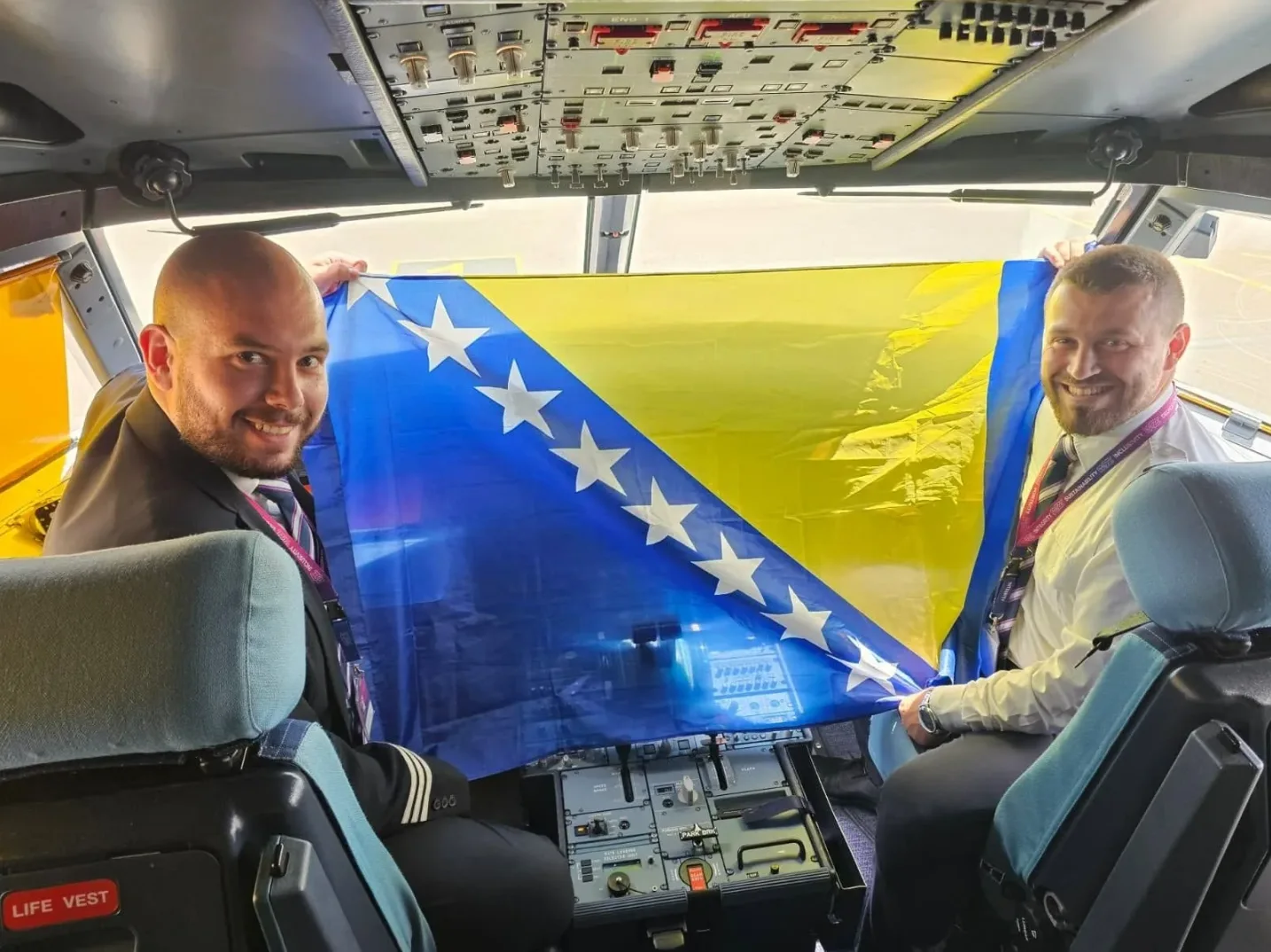 Dva pilota u pilotskoj kabini aviona drže zastavu Bosne i Hercegovine.