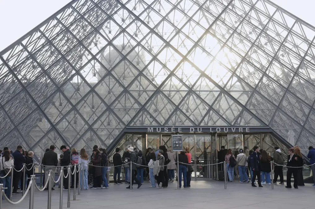 Ljudi čekaju u redu ispred staklene piramide Muzeja Louvre u Parizu.
