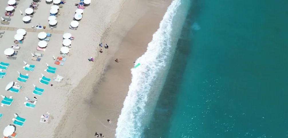 Plaža s brojnim suncobranima, ležaljkama i posjetiocima, s tirkiznim morem koje zapljuskuje obalu.
