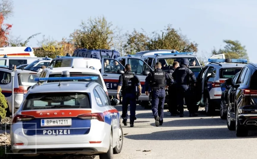 Austrijski policajci u uniformama, neki s prslucima, okupljeni oko policijskih vozila. U prvom planu je policijsko vozilo marke Škoda sa plavim rotacijama, a iza njega se vide druga policijska i sanitetska vozila.