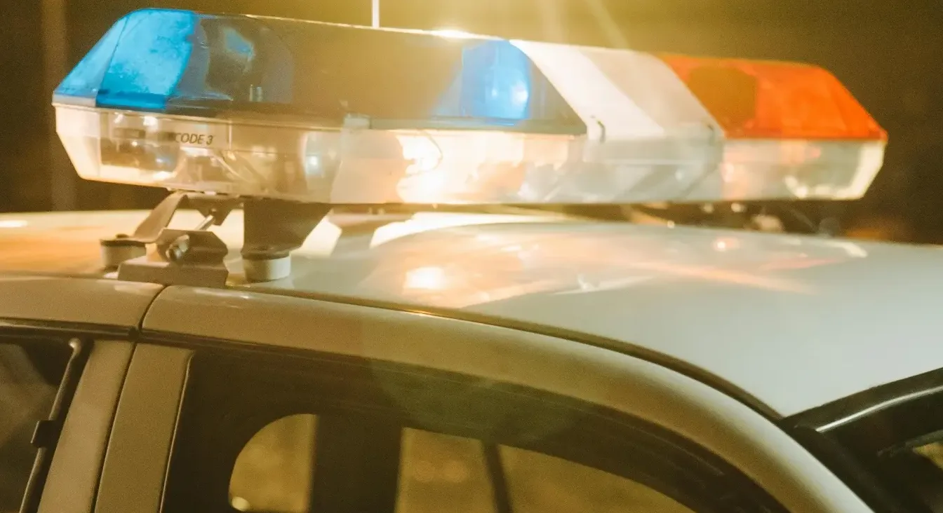 Ugaoni prikaz policijskog automobila s uključenim plavim i crvenim rotacionim svjetlima, u sumrak.