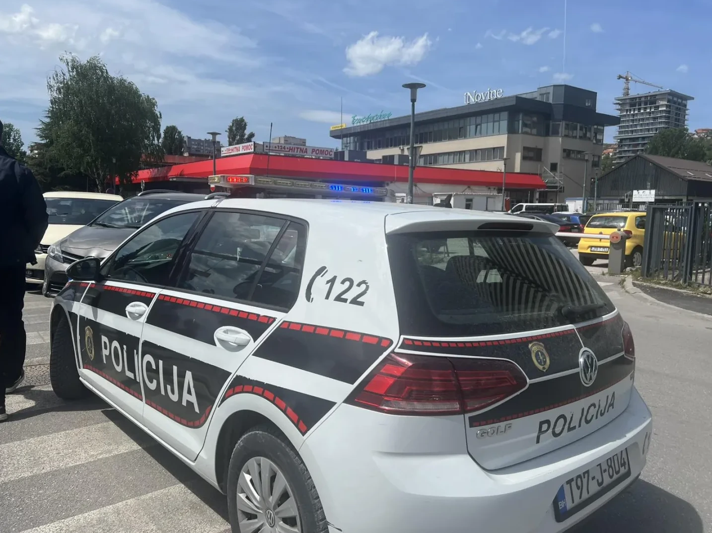 Policijsko vozilo marke Volkswagen Golf sa uključenim rotacionim svjetlima i natpisom "POLICIJA" na boku, parkirano na ulici pored pješačkog prelaza.