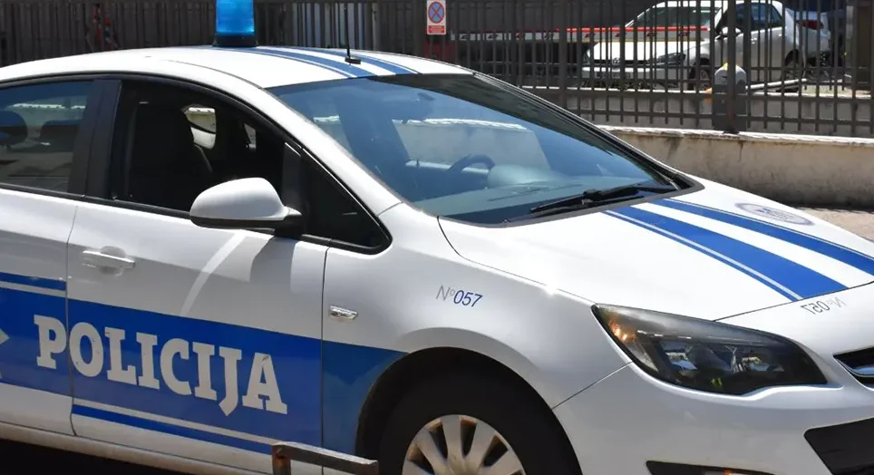 Bijelo policijsko vozilo sa plavom rotacijom na krovu i plavom trakom na boku sa natpisom "POLICIJA".