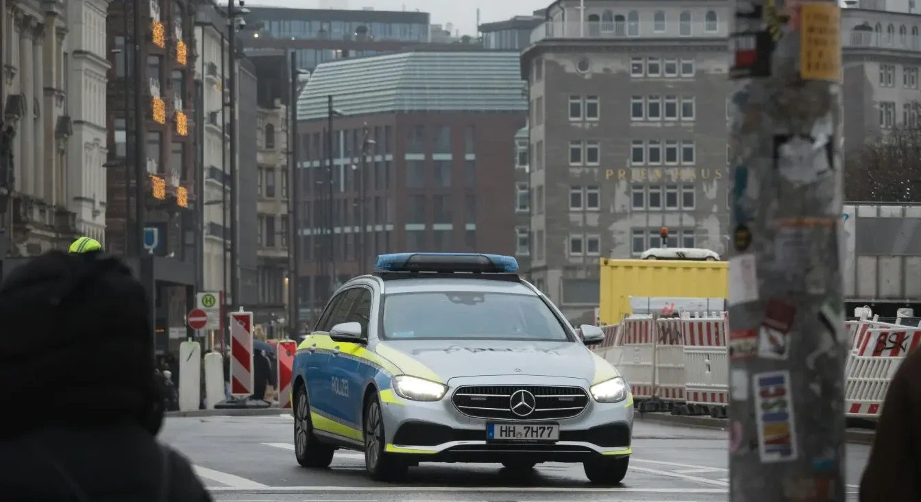 Njemačko policijsko vozilo marke Mercedes-Benz sa uključenim plavim rotacijskim svjetlima vozi gradskom ulicom.