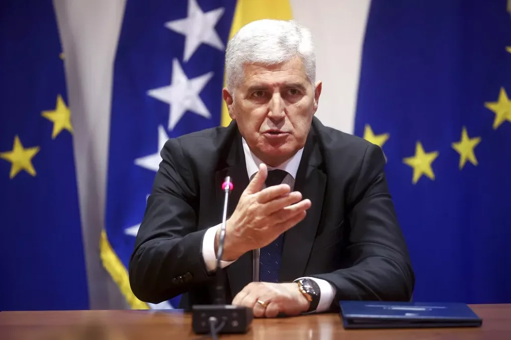 Političar s bijelom košuljom i crnim odijelom sjedi za stolom ispred zastava Evropske Unije i Bosne i Hercegovine.