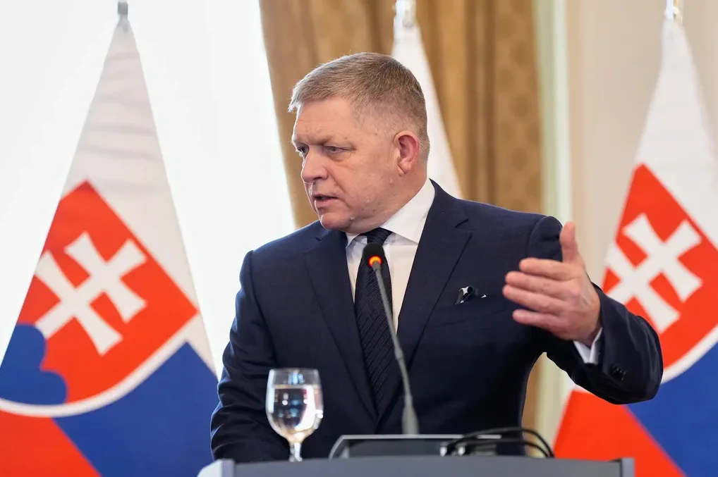 Političar u tamnom odijelu sa bijelom košuljom i tamnom kravatom govori ispred zastave Slovačke.