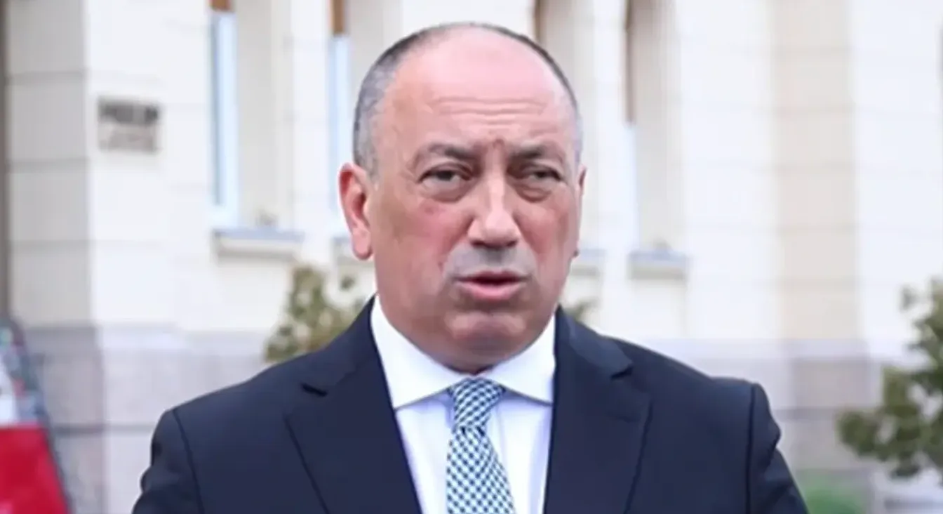 Portret muškarca u tamnom odijelu sa plavo-bijelom kariranom kravatom.
