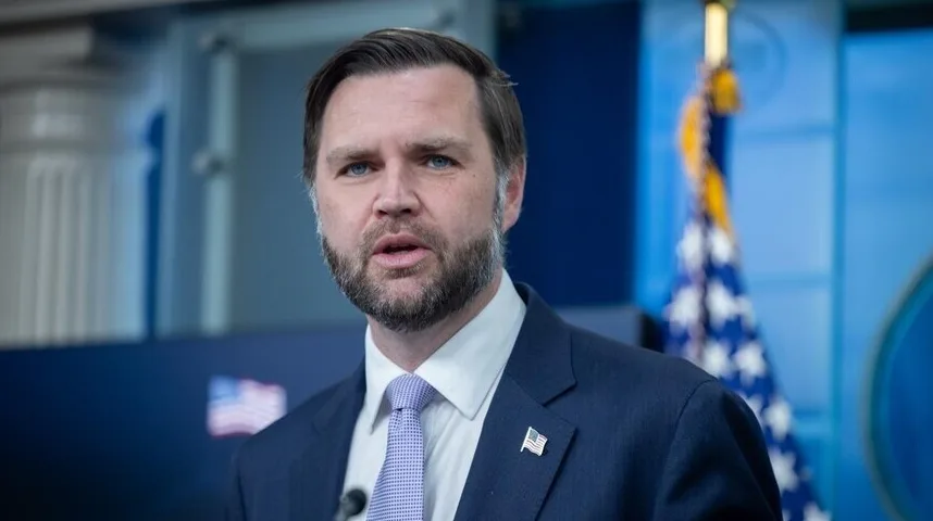 Portret muškarca sa bradom, obučenog u tamni sako i bijelu košulju sa plavom kravatom, sa američkom zastavom u pozadini.