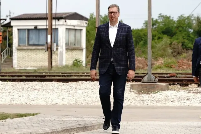 Aleksandar Vučić u tamnom kariranom sakou i farmerkama hoda prugom pored zgrade.