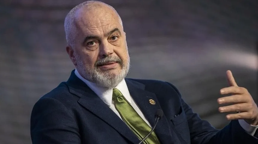 Portret Edija Rame, premijera Albanije, sa sijedom bradom i kosom, obučenog u tamno odijelo i zelenu kravatu, dok govori na sastanku.