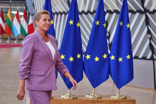Danska premijerka Mette Frederiksen u ljubičastom odijelu hoda ispred zastava Evropske unije.
