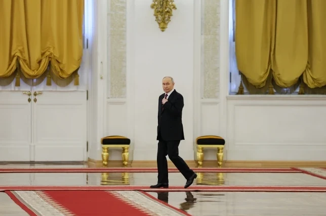 Vladimir Putin u crnom odijelu i crvenoj kravati hoda po crvenom tepihu u svečanoj dvorani.