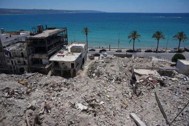 Posljedice razaranja na obali, sa uništenim zgradama i šutom ispred tirkiznog mora i palmi pod vedrim nebom.