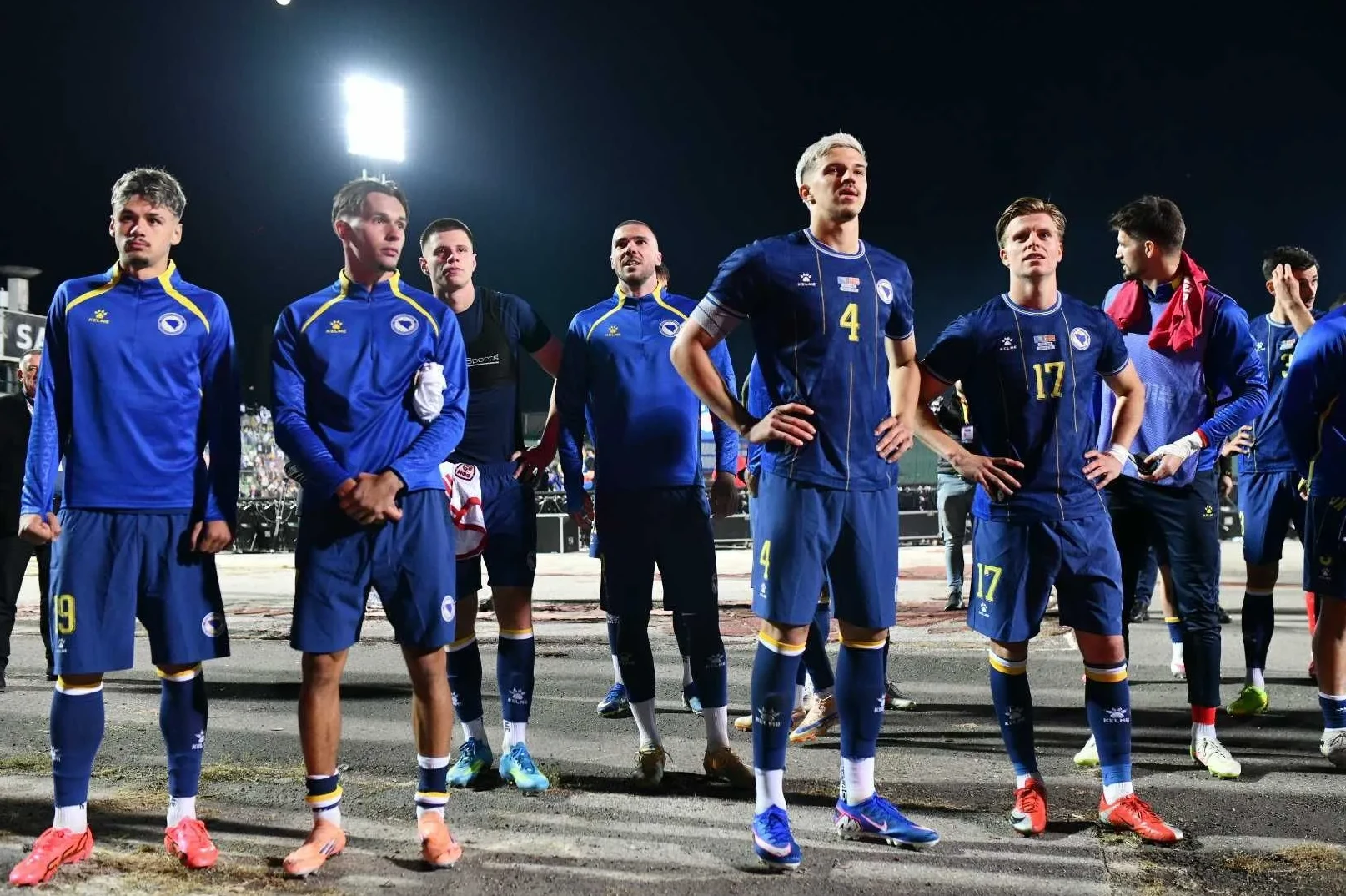 Fudbalska reprezentacija Bosne i Hercegovine u plavim dresovima stoje na terenu.